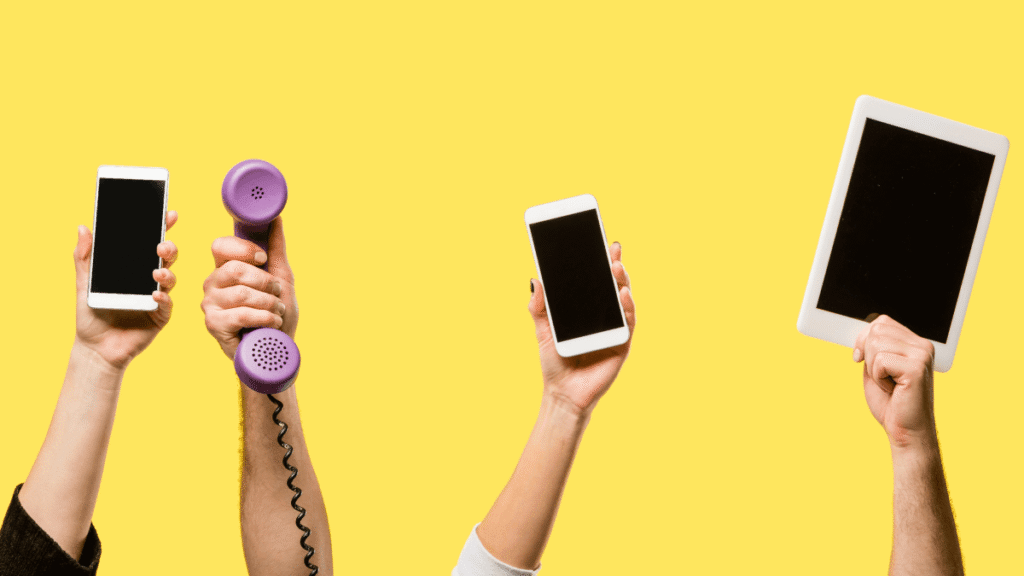 Mains tenant différents appareils (smartphones, tablette, téléphone fixe) sur fond jaune – symbolisant les meilleures applications mobiles pour faciliter les voyages d'affaires.