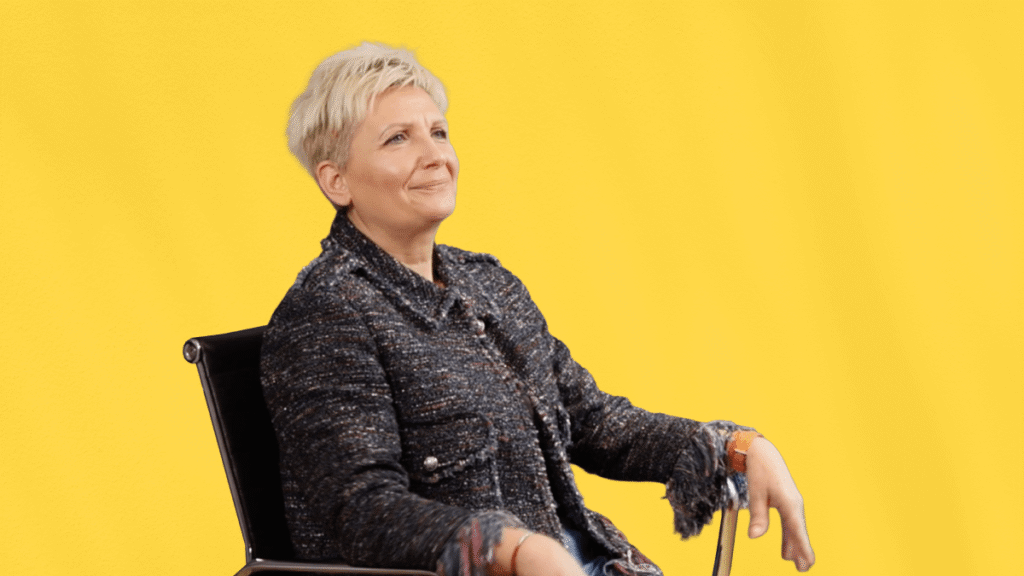 Zedita Trioux, office manager chez CVA France, partage son témoignage client, assise sur une chaise de bureau, en tenue professionnelle, sur fond jaune uni.
