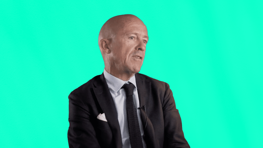 Vincent Truchetto, dirigeant de VTO, en costume cravate, témoigne de son expérience client en gestion des voyages d’affaires, assis sur fond turquoise.