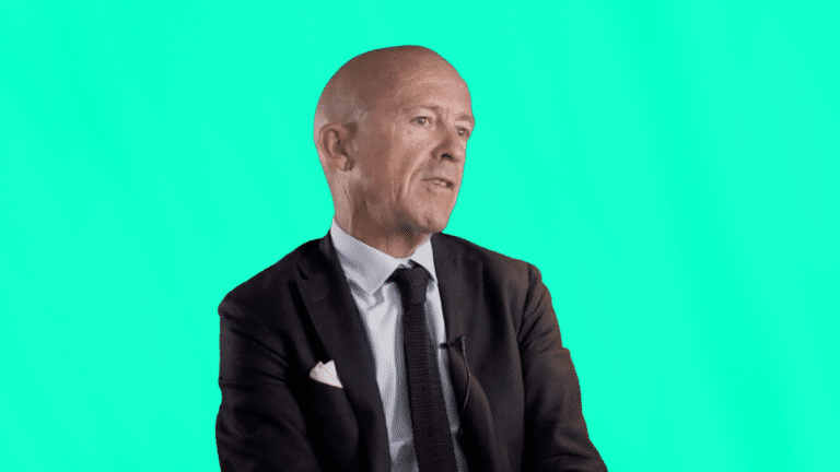 Vincent Truchetto, dirigeant de VTO, en costume cravate, témoigne de son expérience client en gestion des voyages d’affaires, assis sur fond turquoise.