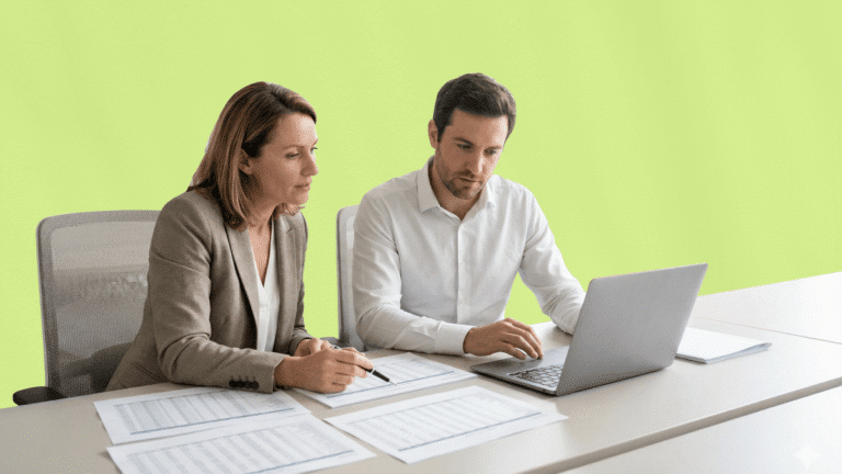 Photographie d'un homme et d'une femme en tenue professionnelle, assis côte à côte devant un ordinateur portable et de nombreux tableaux de données imprimés. Sur un fond vert clair uni, ils analysent avec concentration les propositions reçues. Cette image illustre la phase critique de comparaison des offres et de sélection finale d'une agence de voyages d'affaires.