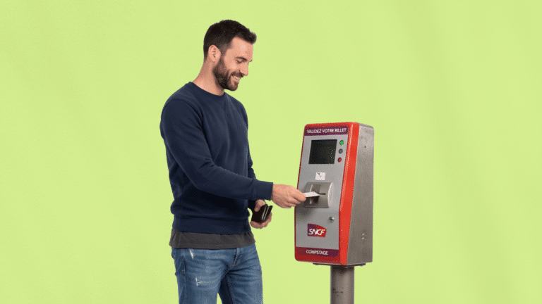 Un homme souriant compostant son billet de train professionnel dans une borne SNCF rouge, sur un fond vert clair.