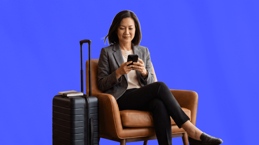 Une femme d'affaires assise à l'aéroport avec sa valise consultant son téléphone connecté aux outils de sécurité et de duty of care voyageuses seules.